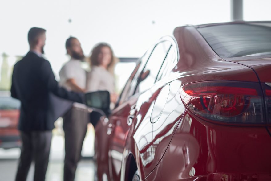 Red Car Close Up, Clients Of Car Dealership Behind.